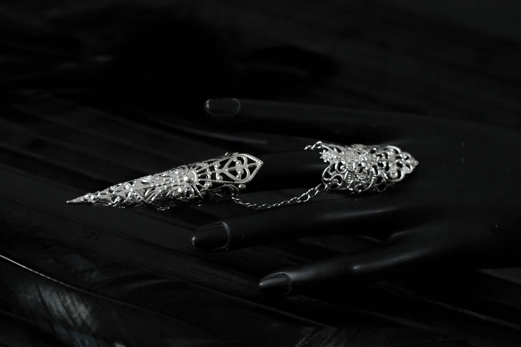 Captured in a dimly lit setting, a mannequin displaying an armor ring, each with elongated, ornate claws. This neo-goth inspired jewelry exudes dark-avantgarde flair, perfect for those with a passion for gothic and alternative styles. The claws are ideal for Halloween, embodying the essence of Gothic-chic, and make a bold statement for witchcore, whimsigoth, or minimal goth fashion. They’re also a striking addition to rave party attire and festival or drag queen jewels.