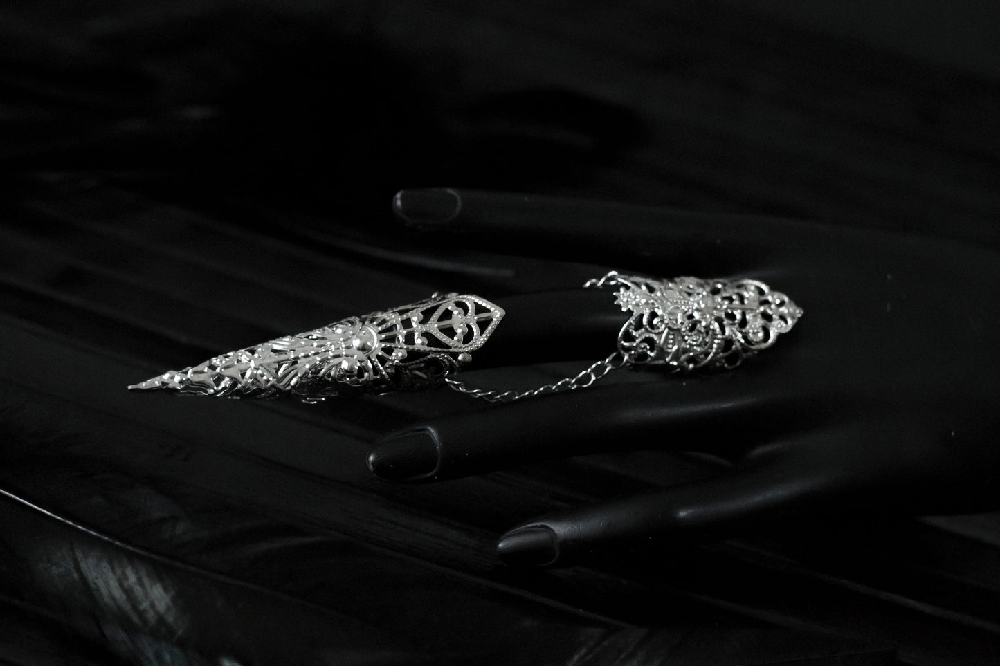 Captured in a dimly lit setting, a mannequin displaying an armor ring, each with elongated, ornate claws. This neo-goth inspired jewelry exudes dark-avantgarde flair, perfect for those with a passion for gothic and alternative styles. The claws are ideal for Halloween, embodying the essence of Gothic-chic, and make a bold statement for witchcore, whimsigoth, or minimal goth fashion. They’re also a striking addition to rave party attire and festival or drag queen jewels.
