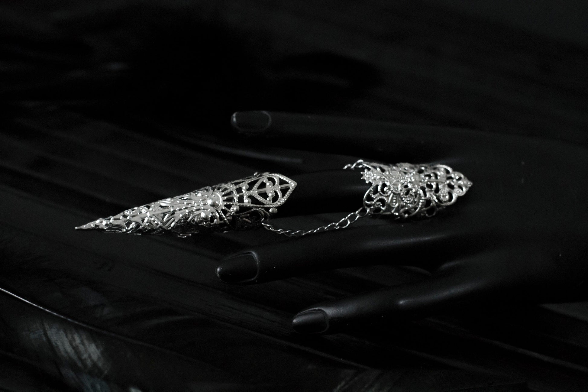 Captured in a dimly lit setting, a mannequin displaying an armor ring, each with elongated, ornate claws. This neo-goth inspired jewelry exudes dark-avantgarde flair, perfect for those with a passion for gothic and alternative styles. The claws are ideal for Halloween, embodying the essence of Gothic-chic, and make a bold statement for witchcore, whimsigoth, or minimal goth fashion. They’re also a striking addition to rave party attire and festival or drag queen jewels.