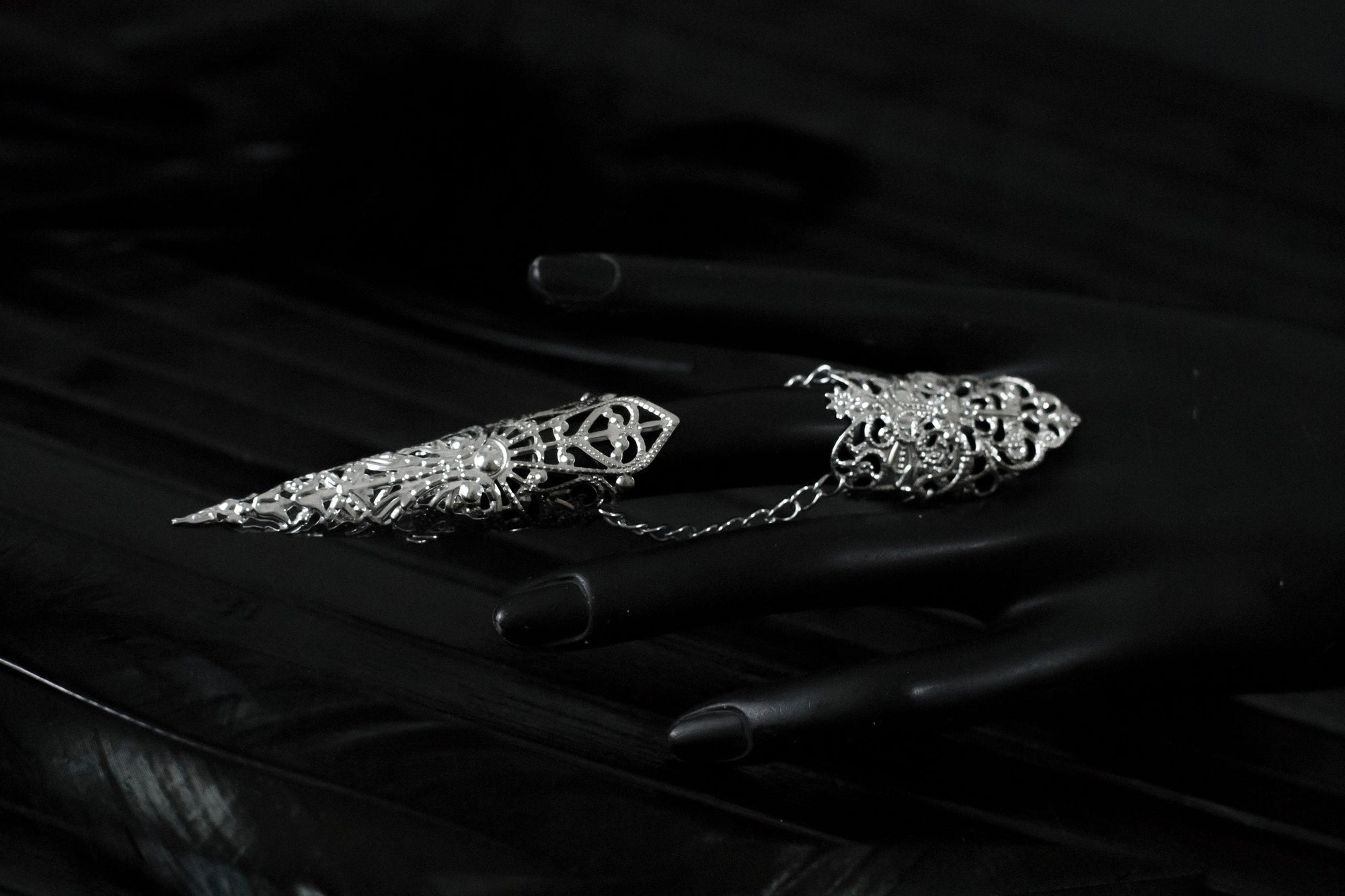 Captured in a dimly lit setting, a mannequin displaying an armor ring, each with elongated, ornate claws. This neo-goth inspired jewelry exudes dark-avantgarde flair, perfect for those with a passion for gothic and alternative styles. The claws are ideal for Halloween, embodying the essence of Gothic-chic, and make a bold statement for witchcore, whimsigoth, or minimal goth fashion. They’re also a striking addition to rave party attire and festival or drag queen jewels.