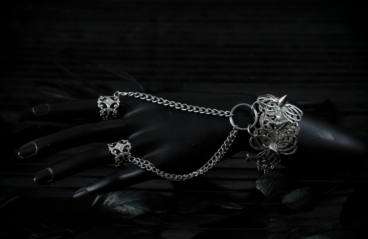 A Myril Jewels punk hand chain bracelet ring with ornate filigree detailing cascades over a black-clad hand, reflecting the brand's mastery in crafting dark avant-garde accessories. Ideal for gothic, Neo Gothic, and alternative styles, this piece is perfect for enhancing Halloween outfits, gothic-chic looks, and Witchcore ensembles. It's also an eye-catching choice for those seeking statement rave party jewelry or festival jewels, offering daily wear versatility for the minimal goth aesthetic