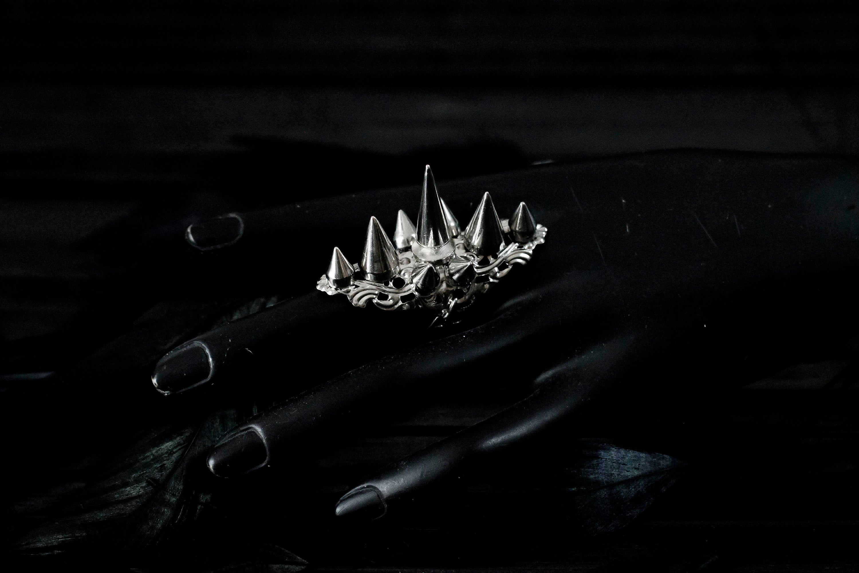 Myril Jewels' punk studded ring is a bold statement piece, meticulously crafted with a fierce array of silver spikes rising in a crown-like silhouette. This ring is a quintessential emblem of Neo Gothic style, designed for those who embody the gothic-chic lifestyle. Ideal for Halloween, it's a standout accessory for everyday wear by those who favor the Witchcore aesthetic, and a must-have for any minimal goth or Whimsigoth-inspired collection