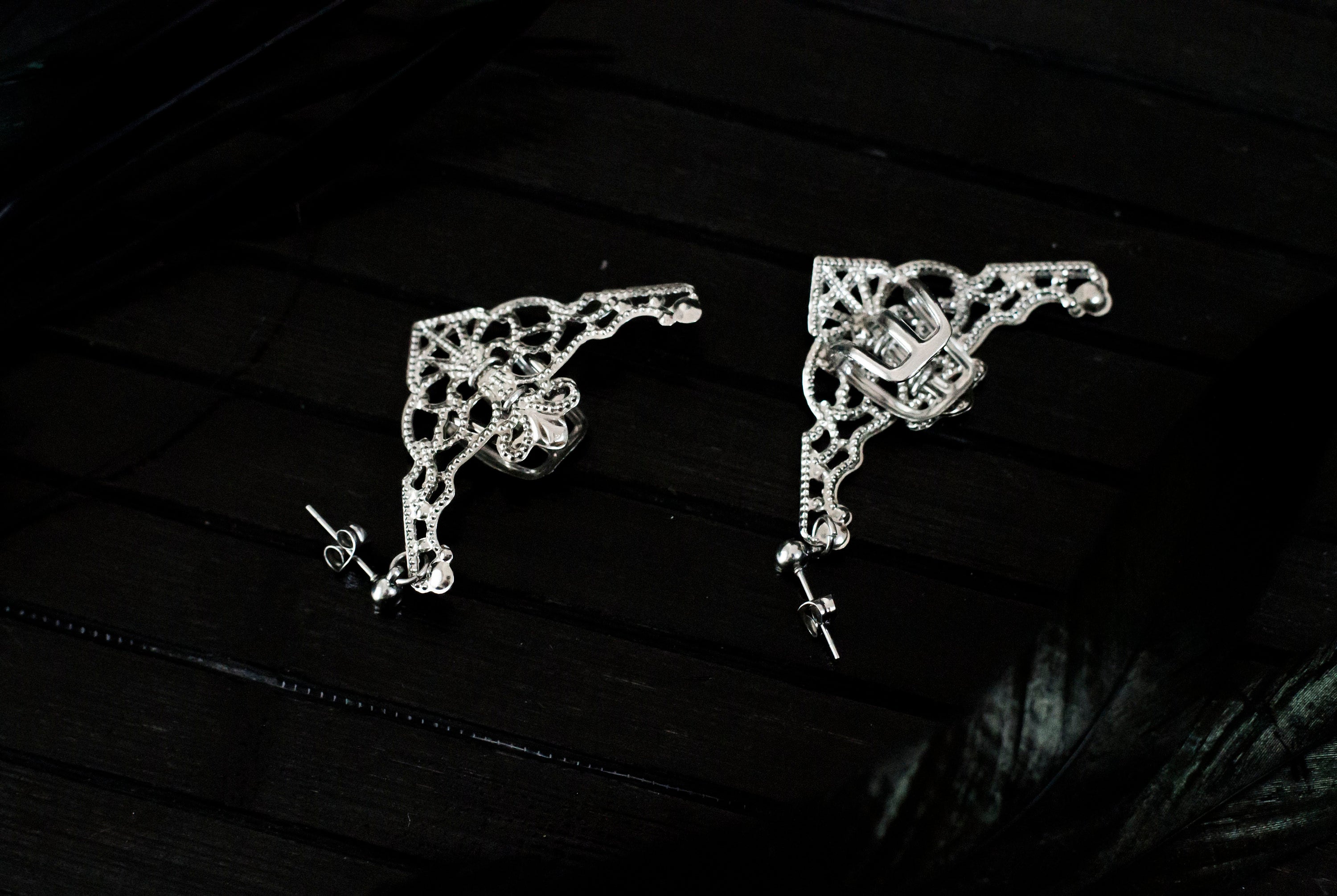Presenting Myril Jewels' intricate cuff earrings, a masterpiece of neo-gothic design. These silver earrings feature an ornate, web-like pattern with a central floral motif, embodying the gothic-chic aesthetic. They dangle gracefully, perfect for adding a touch of whimsigoth elegance to any ensemble. Ideal for those who favor dark-avantgarde accessories, they're versatile for daily wear or as a highlight for rave party attire, encapsulating the essence of festival jewels with a witchcore twist.