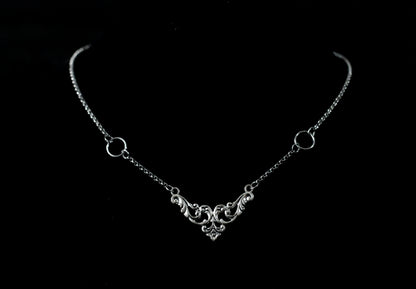 Displayed on a black velvet mannequin is a Myril Jewels elegant gothic necklace, capturing the essence of neo-goth fashion. The necklace, with a fine silver chain, features ornate filigree detailing and symmetrical O-ring accents, embodying the dark-avantgarde aesthetic. This piece is designed for gothic and alternative style aficionados, seamlessly blending with Halloween, punk, and gothic-chic ensembles, and is a sophisticated choice for whimsigoth, witchcore, or minimal goth everyday wear