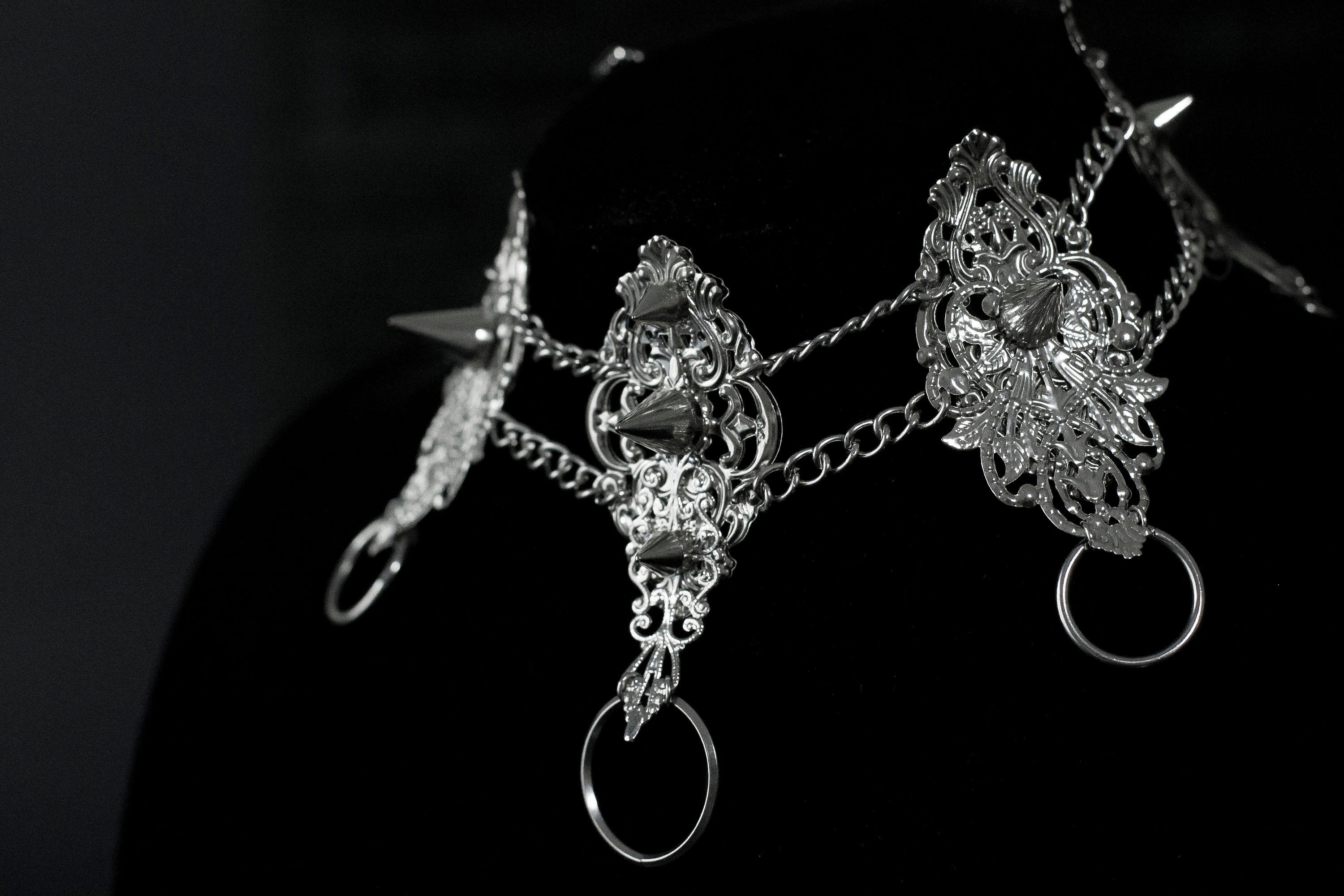 This Myril Jewels dark avant-garde metal choker, featuring punk studded details, is an exquisite piece for gothic fashion aficionados. Its intricate filigree and chain design showcase the brand's commitment to handcrafted Neo Gothic elegance. Ideal for Gothic Lolita, Gothic-chic, or whimsigoth wardrobes, it's a statement accessory for Halloween and everyday minimal goth style, exuding witchcore vibes