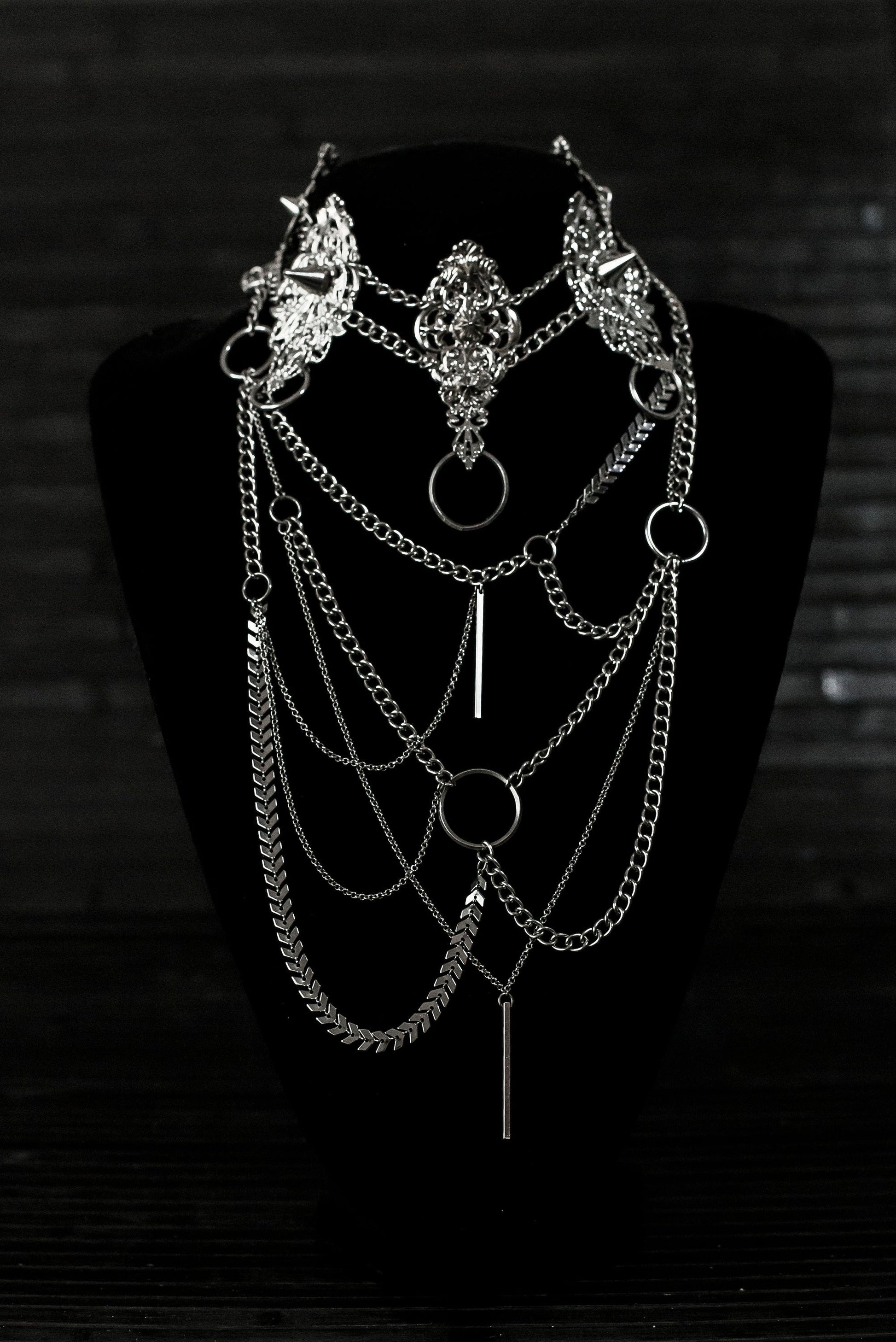 Myril Jewels presents an exquisite punk studded metal choker paired with a multi-layer long chain necklace, embodying the dark avant-garde spirit. This Italian handcrafted ensemble is a testament to the fusion of Neo Gothic flair and Gothic-chic, perfect for Halloween, everyday wear, or any whimsigoth and witchcore inspired look. The layered chains add depth to the minimal goth aesthetic, making it a versatile statement piece for alternative style connoisseurs