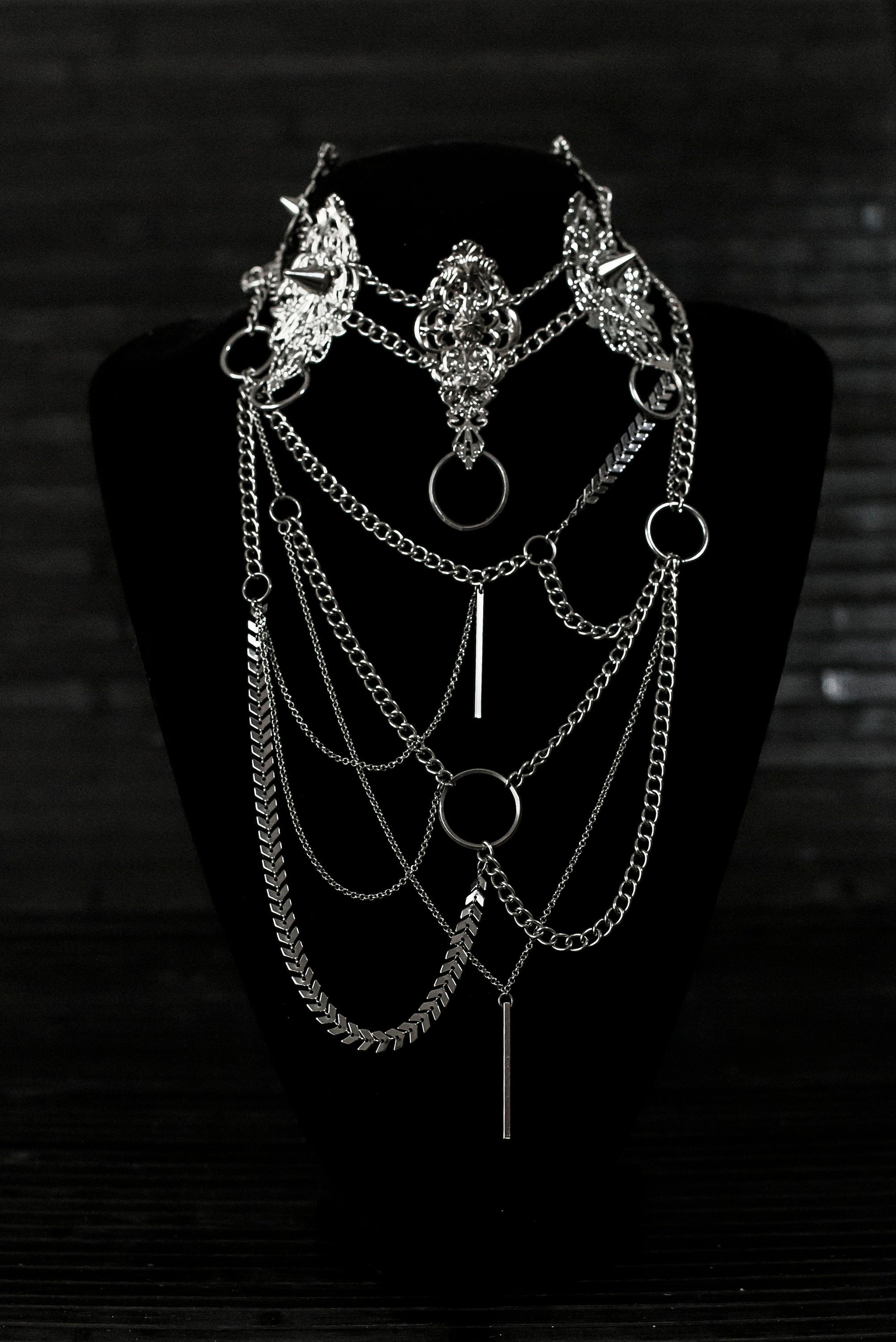 Myril Jewels presents an exquisite punk studded metal choker paired with a multi-layer long chain necklace, embodying the dark avant-garde spirit. This Italian handcrafted ensemble is a testament to the fusion of Neo Gothic flair and Gothic-chic, perfect for Halloween, everyday wear, or any whimsigoth and witchcore inspired look. The layered chains add depth to the minimal goth aesthetic, making it a versatile statement piece for alternative style connoisseurs