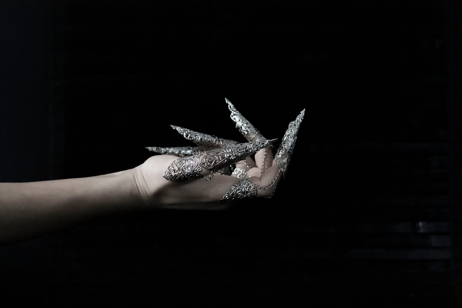A hand is strikingly adorned with a full set of Myril Jewels rings, each extending into long, ornate claws that exemplify a dramatic neo-goth style. Crafted with intricate silver detailing, these rings are perfect for dark-avantgarde enthusiasts and make a bold statement piece for Halloween, punk events, and drag queen performances. They also complement a gothic-chic, whimsigoth, or witchcore aesthetic, suitable for everyday wear, and are a dazzling addition to rave party and festival jewelry collections.