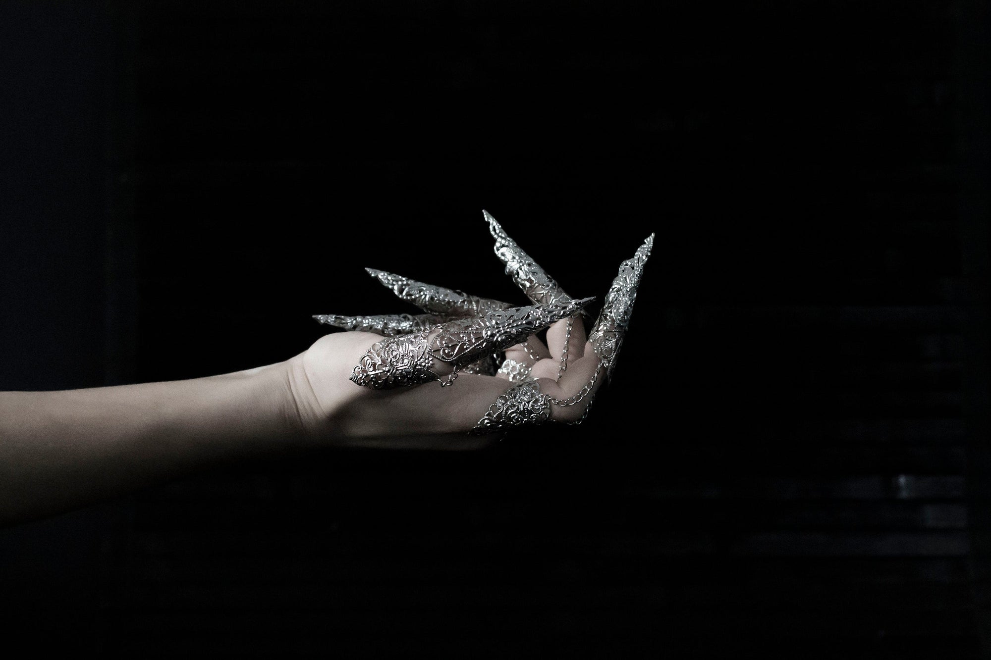 A hand is strikingly adorned with a full set of Myril Jewels rings, each extending into long, ornate claws that exemplify a dramatic neo-goth style. Crafted with intricate silver detailing, these rings are perfect for dark-avantgarde enthusiasts and make a bold statement piece for Halloween, punk events, and drag queen performances. They also complement a gothic-chic, whimsigoth, or witchcore aesthetic, suitable for everyday wear, and are a dazzling addition to rave party and festival jewelry collections.