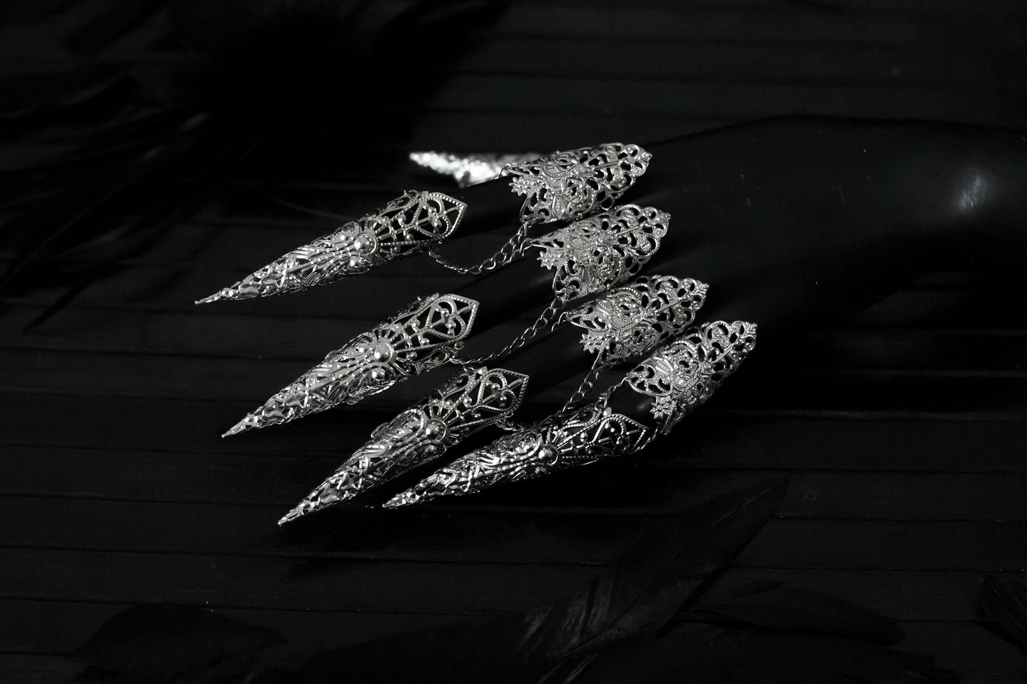Captured in a dimly lit setting, a mannequin displaying a full set of Myril Jewels armor rings, each with elongated, ornate claws. This neo-goth inspired jewelry exudes dark-avantgarde flair, perfect for those with a passion for gothic and alternative styles. The claws are ideal for Halloween, embodying the essence of Gothic-chic, and make a bold statement for witchcore, whimsigoth, or minimal goth fashion. They’re also a striking addition to rave party attire and festival or drag queen jewels.