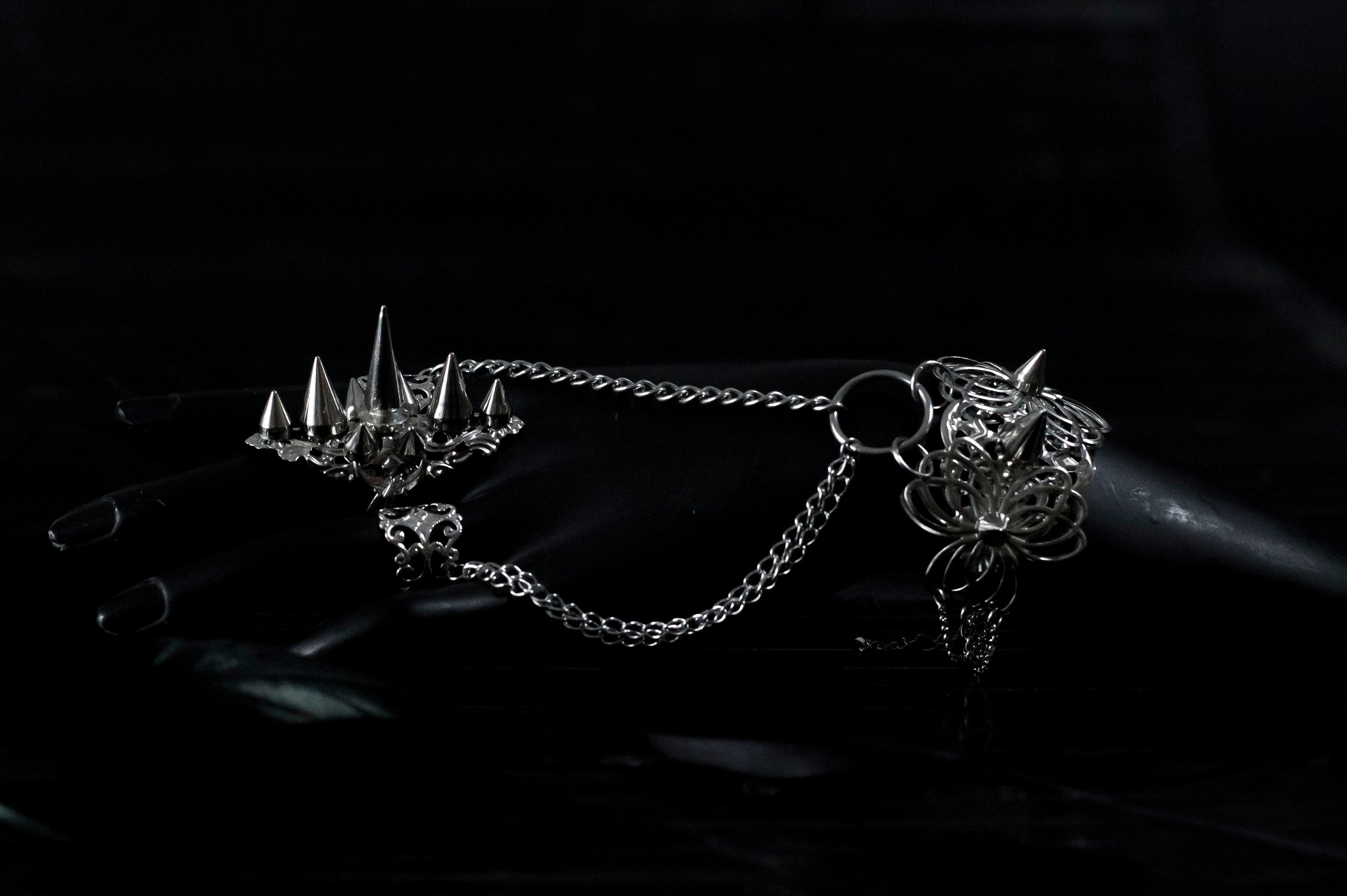 Capture the essence of punk rebellion with Myril Jewels' edgy studded ring and matching hand chain bracelet ring. These bold statement pieces, with its sharp studs and metallic finish, are a must-have for lovers of dark-avantgarde and gothic accessories. Ideal for Halloween, it also complements everyday minimal goth looks, Witchcore styles, and Gothic-chic ensembles, offering a versatile addition to any Neo Gothic jewel collection