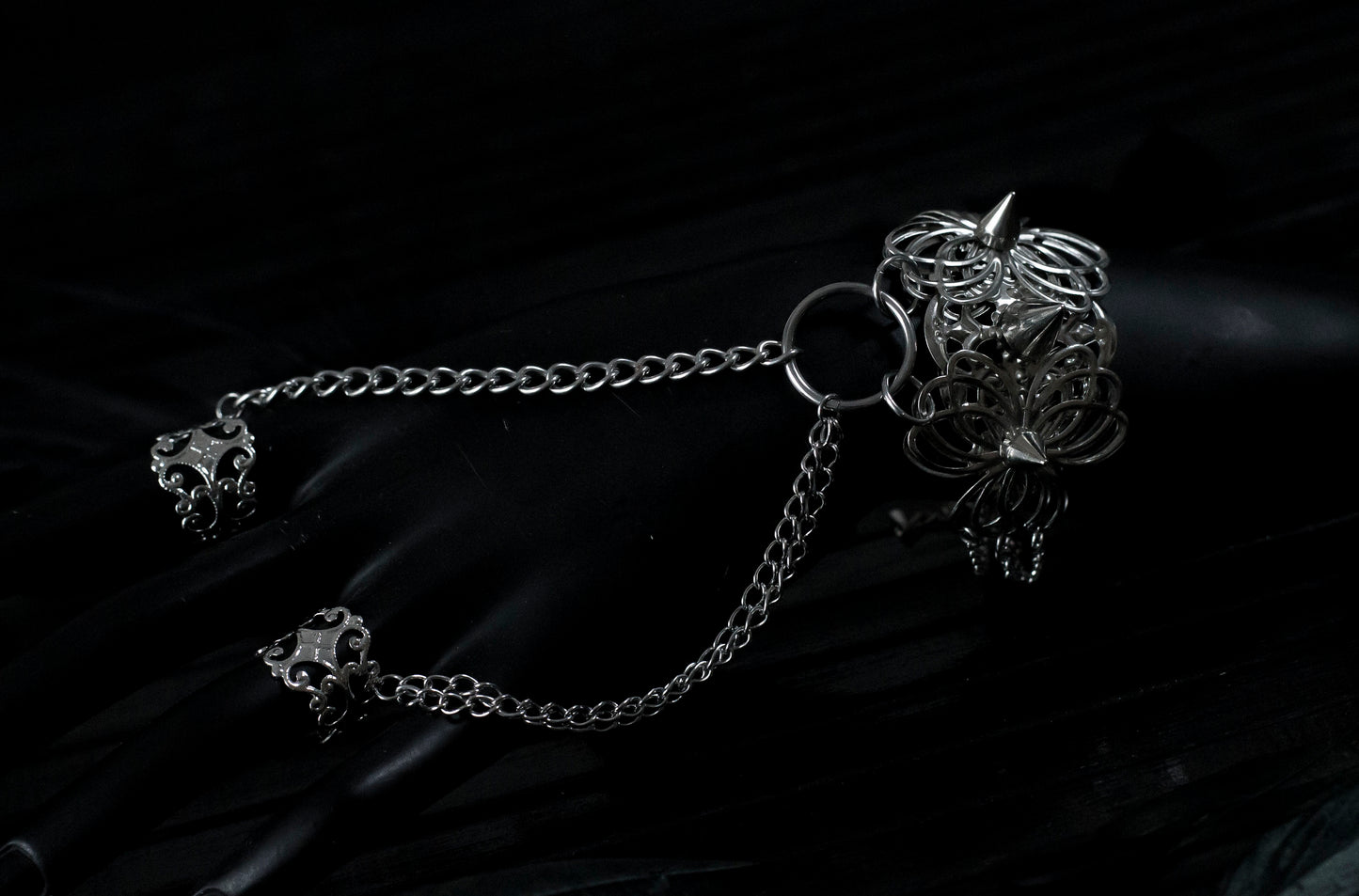 A Myril Jewels punk hand chain bracelet ring with ornate filigree detailing cascades over a black-clad hand, reflecting the brand's mastery in crafting dark avant-garde accessories. Ideal for gothic, Neo Gothic, and alternative styles, this piece is perfect for enhancing Halloween outfits, gothic-chic looks, and Witchcore ensembles. It's also an eye-catching choice for those seeking statement rave party jewelry or festival jewels, offering daily wear versatility for the minimal goth aesthetic