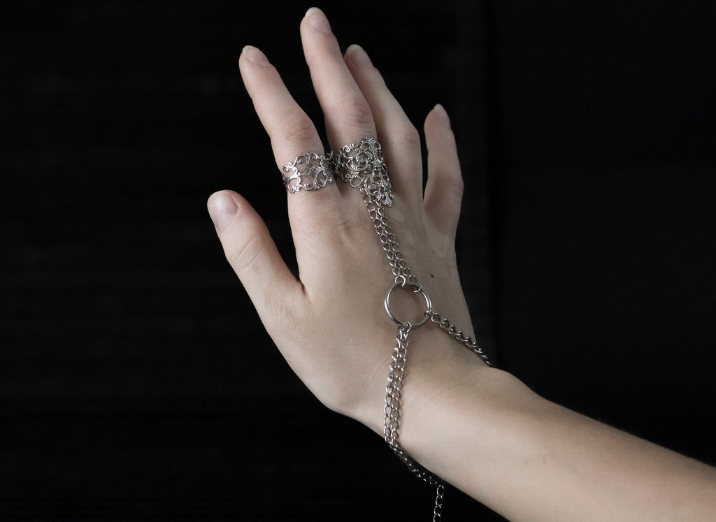 Elevate your gothic-chic style with this Myril Jewels hand chain bracelet ring, designed for the sophisticated avant-garde enthusiast. This piece features an intricate filigree design, exuding a dark, elegant allure perfect for everyday wear or a rave party statement. Crafted with the whimsigoth aesthetic in mind, the striking contrast of the shiny silver against the model's black stiletto nails encapsulates a neo-gothic vibe, making it a timeless addition to any witchcore or minimal goth jewelry collectio