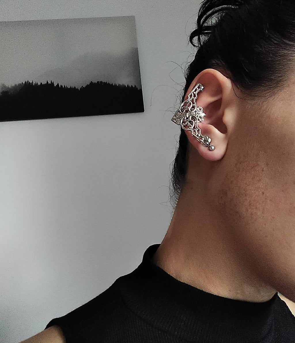 A close-up view of a model wearing Myril Jewels' cuff earrings, which are masterfully crafted in a rich gold tone. The detailed filigree design evokes a neo-gothic aesthetic, perfect for those who desire a touch of dark-avantgarde elegance. These earrings are ideal for gothic-chic fashion lovers, adding a unique statement to both everyday wear and special occasions like Halloween, and are versatile enough for festival adornment or as part of a minimal goth wardrobe.