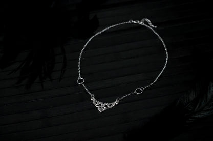 Displayed on a black layer is a Myril Jewels elegant gothic necklace, capturing the essence of neo-goth fashion. The necklace, with a fine silver chain, features ornate filigree detailing and symmetrical O-ring accents, embodying the dark-avantgarde aesthetic. This piece is designed for gothic and alternative style aficionados, seamlessly blending with Halloween, punk, and gothic-chic ensembles, and is a sophisticated choice for whimsigoth, witchcore, or minimal goth everyday wear