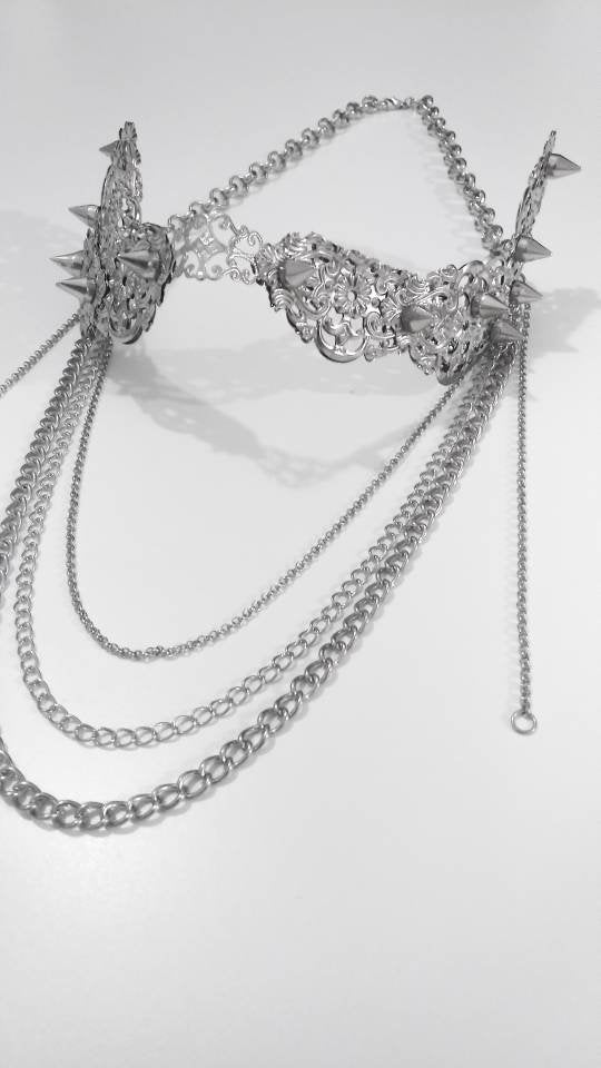 An intricate Myril Jewels nose mask lies against a stark white backdrop, its studded surface and delicate filigree work exuding dark-avantgarde sophistication. Cascading chains add a dramatic touch, reflecting the brand’s neo-gothic essence. This piece is a perfect accessory for gothic-chic style, blending in with whimsigoth and witchcore trends, and is suitable for Halloween, everyday fashion, or as a bold statement at rave parties and festivals