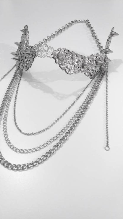 An intricate Myril Jewels nose mask lies against a stark white backdrop, its studded surface and delicate filigree work exuding dark-avantgarde sophistication. Cascading chains add a dramatic touch, reflecting the brand’s neo-gothic essence. This piece is a perfect accessory for gothic-chic style, blending in with whimsigoth and witchcore trends, and is suitable for Halloween, everyday fashion, or as a bold statement at rave parties and festivals