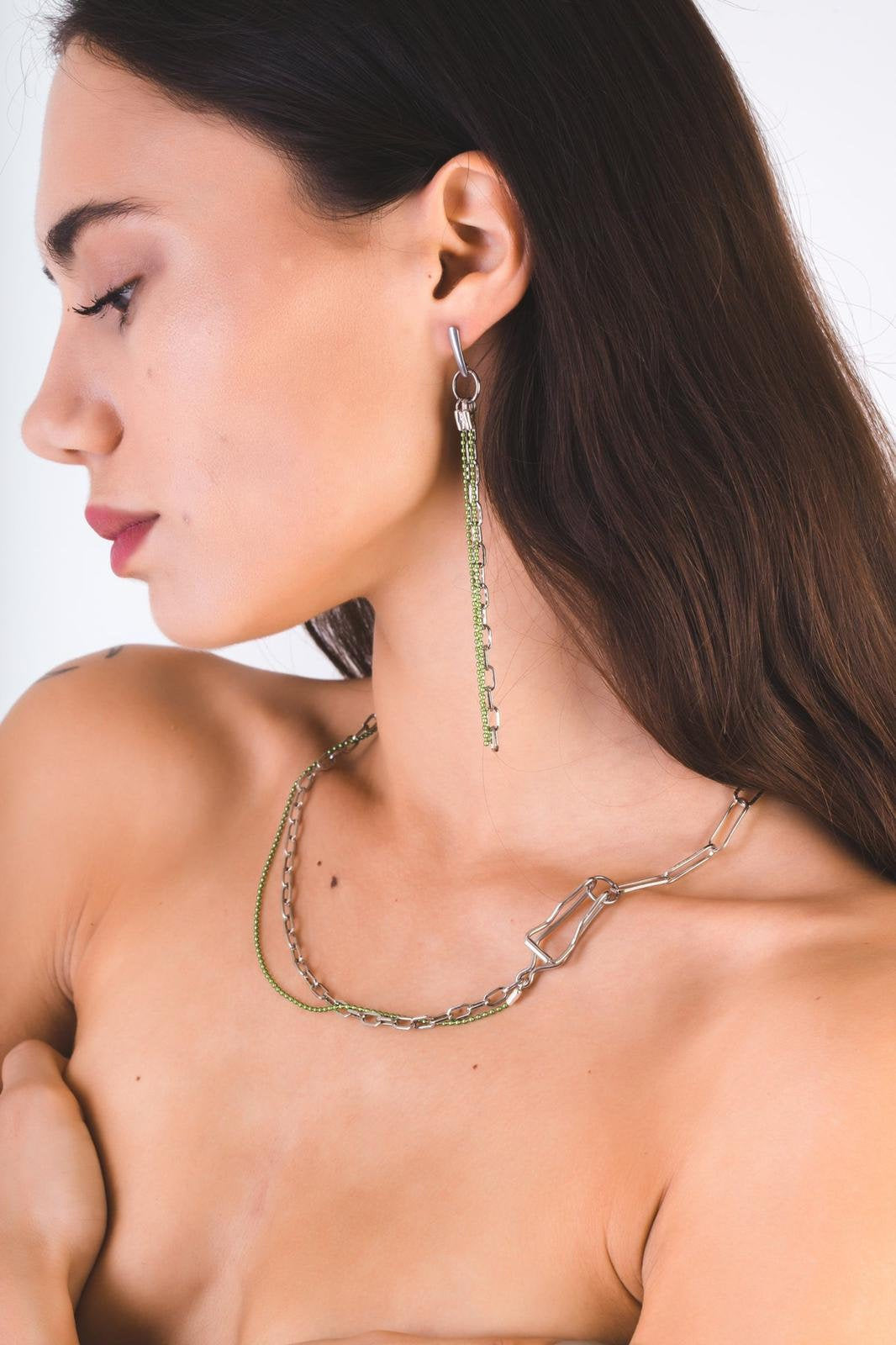 A model showcases a Myril Jewels punk necklace featuring silver and green chains with a unique, edgy design. The necklace embodies the brand's dark-avantgarde ethos, perfect for those drawn to neo-gothic and gothic-chic styles. This piece is versatile enough for Halloween, witchcore, or everyday wear, and adds an unconventional touch to any rave party or festival ensemble