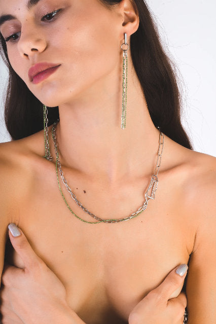 A model showcases a Myril Jewels punk necklace, featuring silver and green chains with a unique, edgy design. This piece represents the brand's neo-gothic aesthetic, aligning with the tastes of those who admire dark-avantgarde, gothic-chic jewelry. The necklace's bold style makes it suitable for Halloween, witchcore fashion, and is an eye-catching addition to the minimal goth wardrobe, perfect for rave parties and festival events.