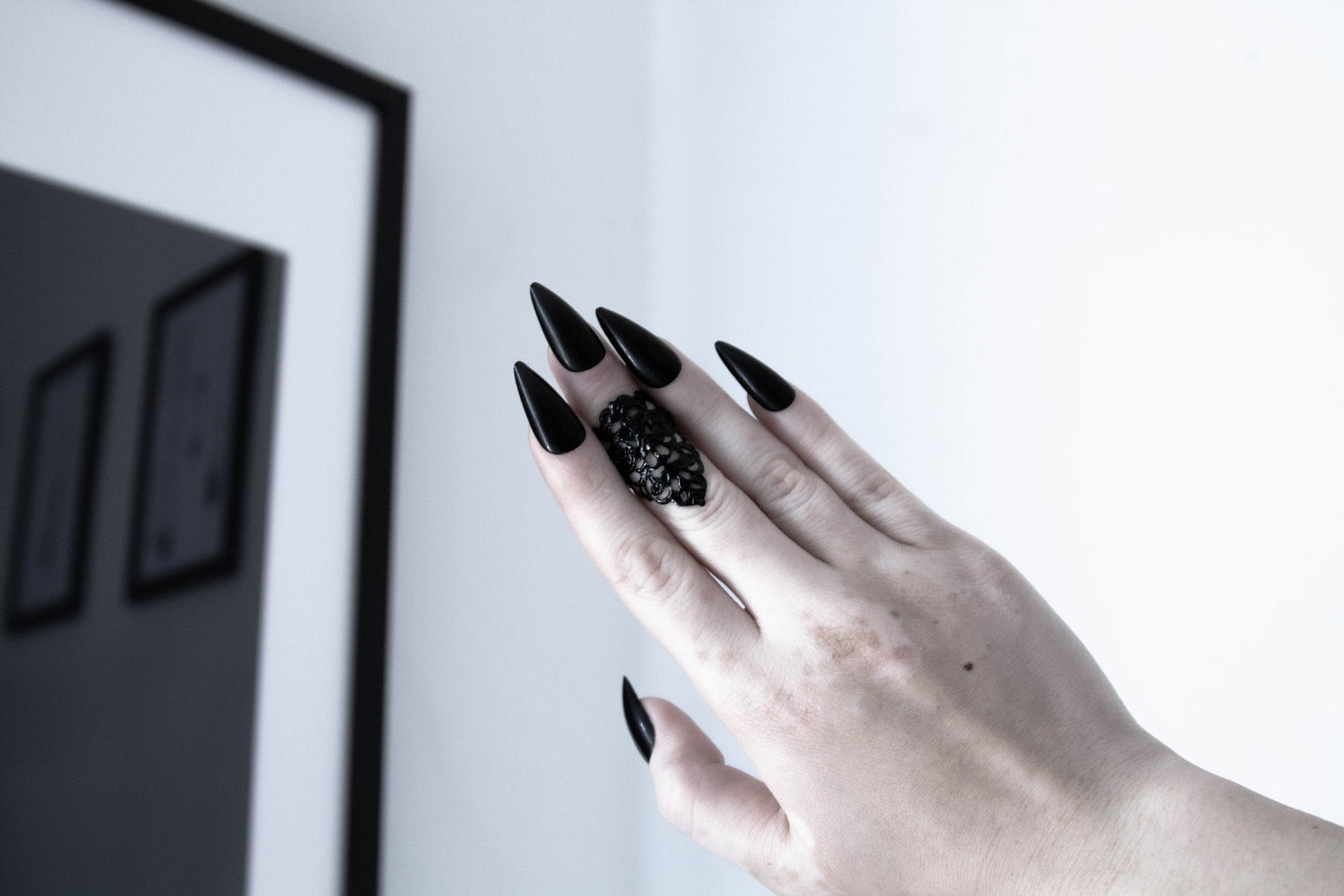 A hand presents a Myril Jewels neo-goth midi ring, embodying a dark-avantgarde style ideal for gothic and alternative fashion enthusiasts. The ring's elaborate texture and intricate design speak to the brand's signature gothic-chic aesthetic, making it a perfect accessory for everyday wear or as a statement piece for Halloween. Its bold, whimsigoth charm is complemented by the wearer's long, sleek black nails, enhancing its witchcore appeal, suitable for rave parties, festivals