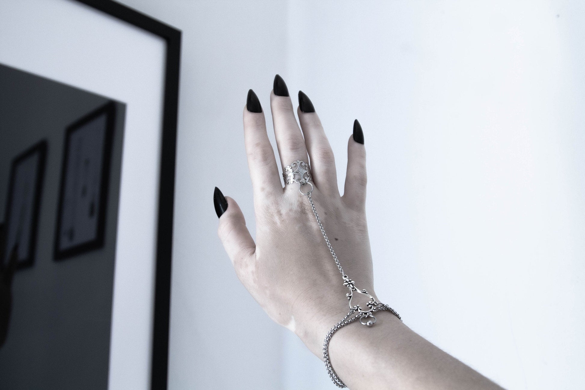 A delicate hand chain bracelet ring graces a slender hand, exemplifying Myril Jewels' dark avant-garde style. This neo-gothic accessory, with its intricate design, is perfect for adding a touch of gothic-chic to any outfit, whether it's for everyday sophistication or a striking festival or Halloween look.