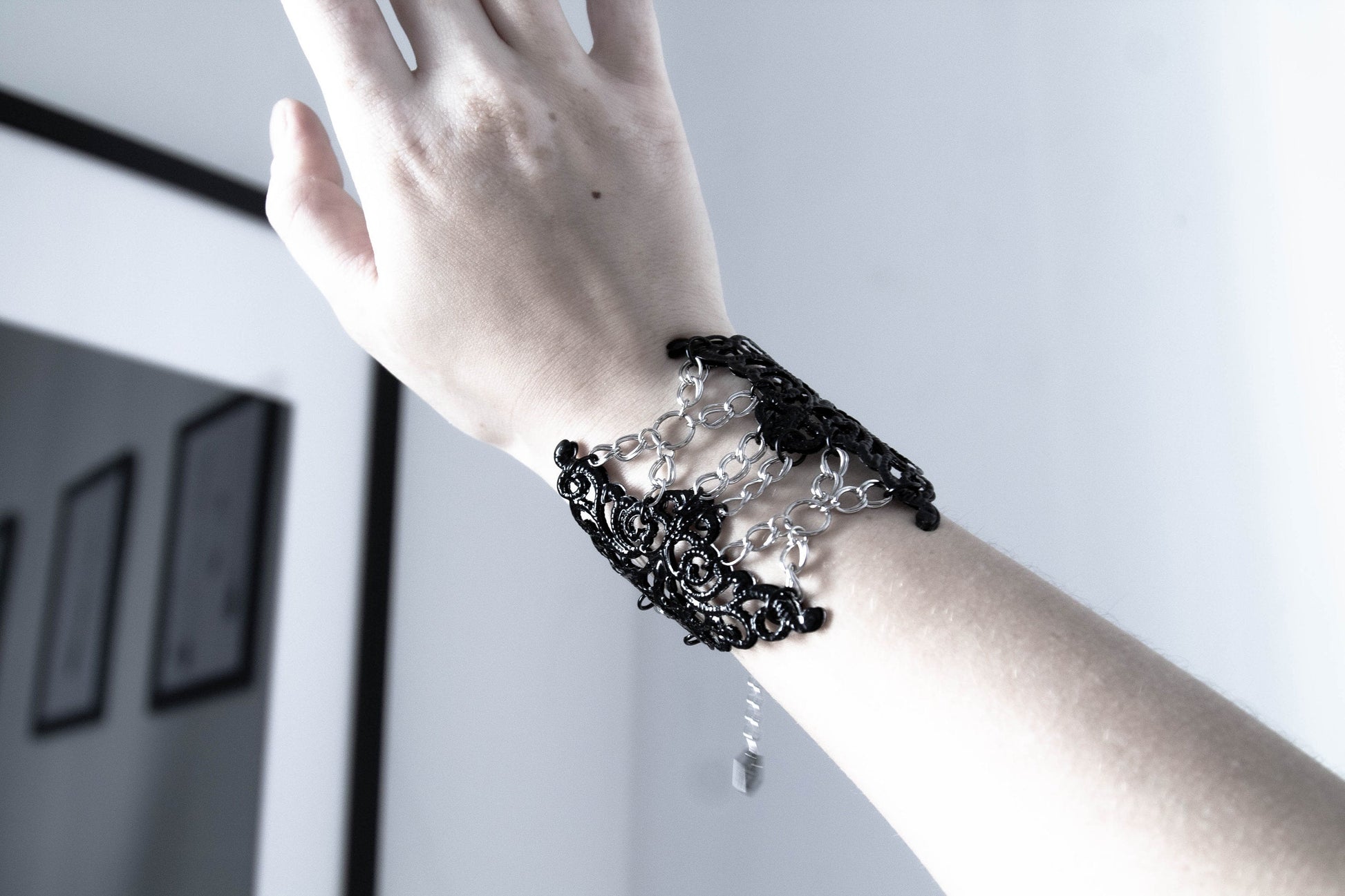 A model’s wrist is adorned with a Myril Jewels gothic bracelet featuring intricate, dark filigree that interlaces to form a lavish, ornamental design. This piece embodies the spirit of neo-gothic jewelry, a bold accessory suited for Witchcore enthusiasts, and a striking gift for those with a penchant for gothic-chic or festival fashion.
