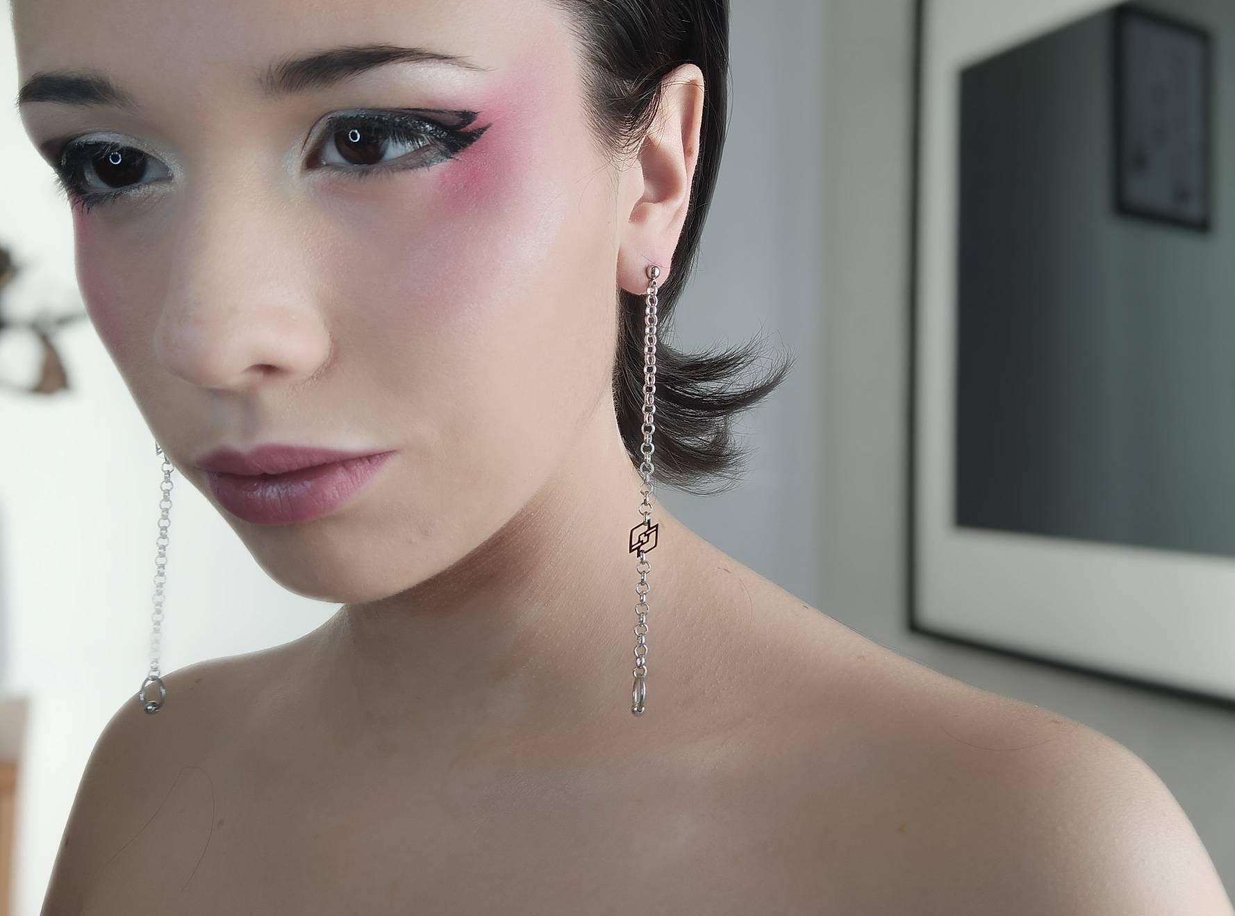 A model presents Myril Jewels' signature long chain earrings, each featuring the iconic black Myril logo. These earrings capture the brand's dark avant-garde essence, ideal for gothic, punk, and alternative fashion aficionados, and versatile enough for Halloween, festival wear, or daily minimalist goth style