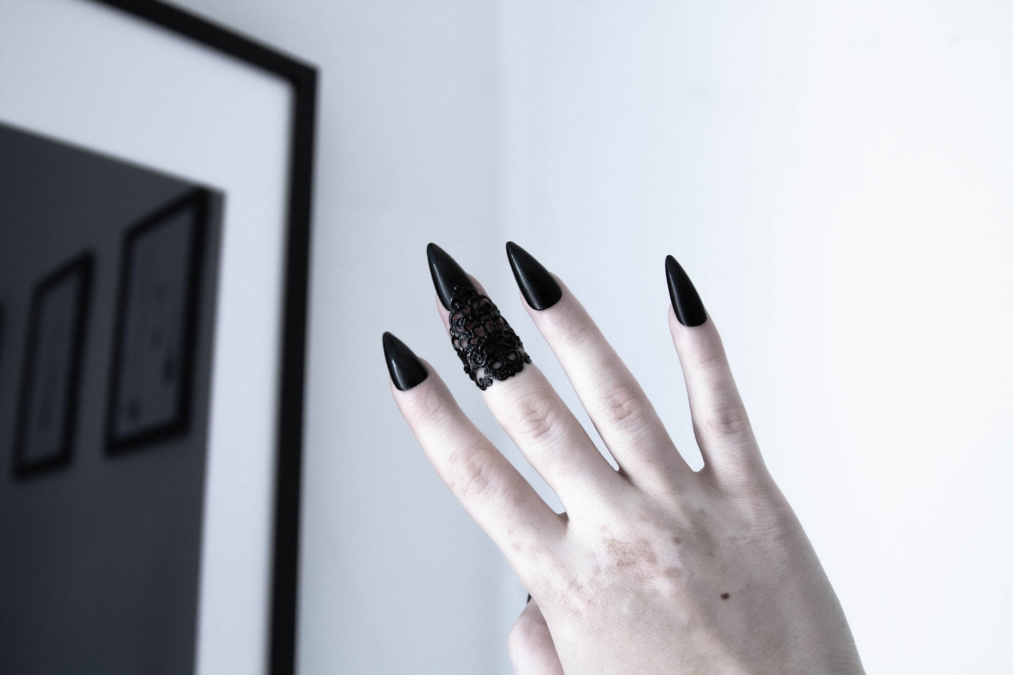 A hand flaunts a Myril Jewels goth midi ring, its dark, intricate lattice design embodying neo-gothic sophistication. The ring, perfect for Halloween or as a statement piece for everyday wear, complements the wearer's long, sleek black nails, enhancing the gothic-chic allure. This accessory captures the essence of dark-avantgarde style, making it an ideal choice for those who cherish punk jewelry, whimsigoth aesthetics, or wish to add an edgy touch to their festival jewels collection