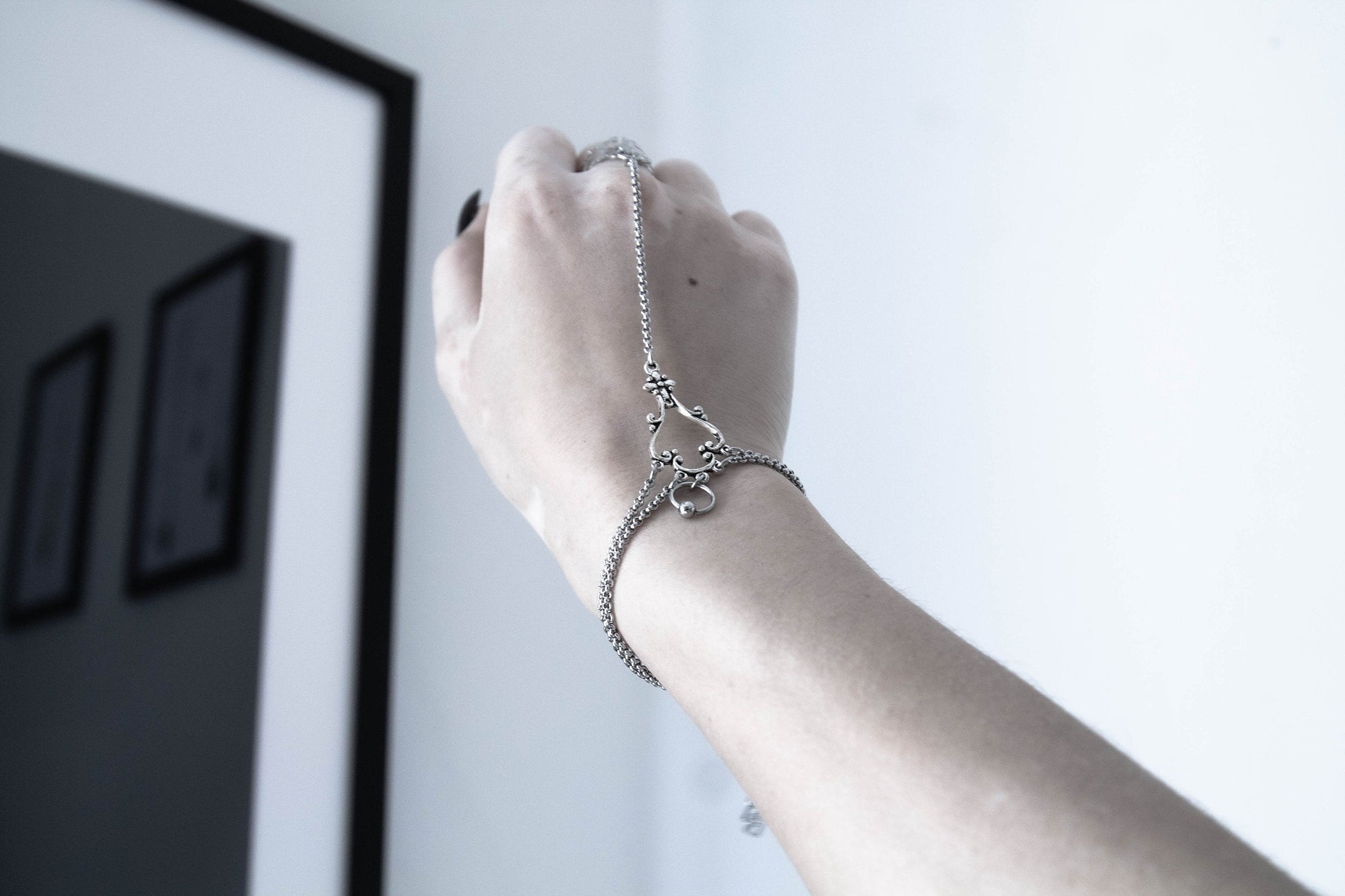 A hand showcases a Myril Jewels slave bracelet ring with delicate chain connections, a blend of neo-gothic charm and dark elegance, ideal for those who embrace a gothic-chic lifestyle.